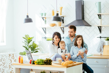 Young mother, father and two children cooking in a kitchen. Parents and kids cook dinner. Family...