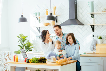 Happy young family with Mum, Dad and two different age children cooking in the kitchen preparing a salad meal together.
