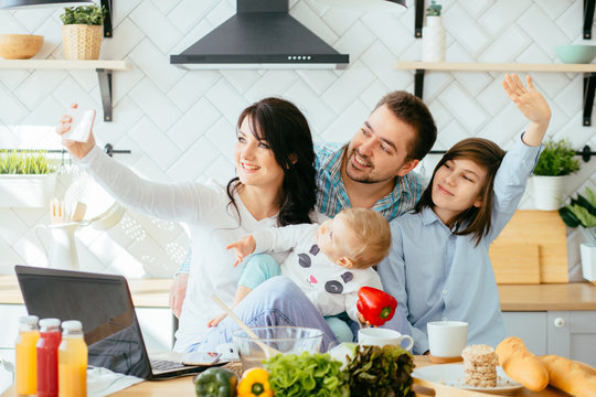 Happy young family with two funny children taking selfie on kitchen while having breakfast