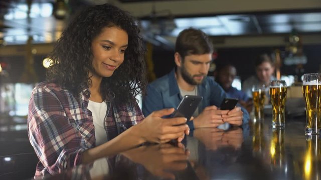 Young people using phones in bar, ignoring live communication, addiction concept