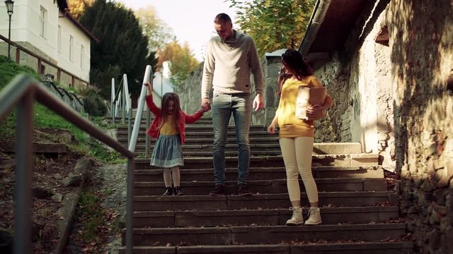 A young family with small daughter walking down the stairs outdoors in town.