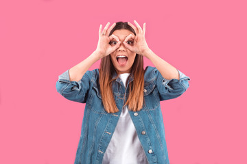 a young girl made her hands glasses on her eyes on a pink background