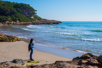 Side view of a young woman wearing casual clothes standing on the beach while looking away to the horizon in a bright day