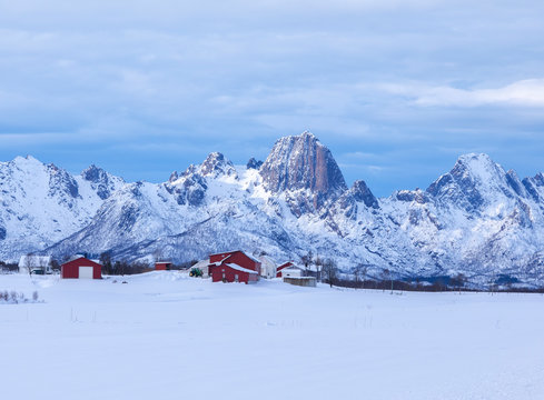 Farm and tipical Norwegian houses called rorbu surronded by snow frames the snowy peaks of Mount Raeka  Holmstad Bo Vester&aring;len Nordland county Norway