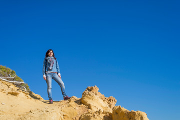 Side view of young woman wearing casual clothes standing on the beach while looking away to the horizon in a bright day