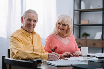 happy senior couple sitting at table and filling documents at home