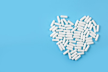 White pills forming heart shape on blue background. Medical care concept.