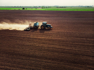 Tractor cultivating field, kicking up rocks and dust in early morning