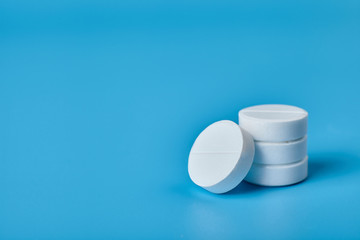 White pills and white bottle on blue background, close up.