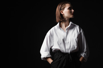 Portrait of an elegant young woman in a white shirt and black pants. Interesting studio light