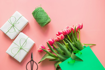 Gifts and red tulip flowers in green paper bag on pink. Spring. Mother day.