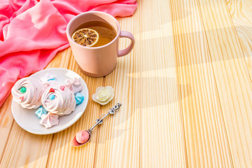 Romantic sweet breakfast concept. Green tea, lemon, meringue (cake). On wooden background with pink cloth.