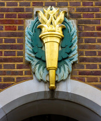 Golden torch with flames carved in stone with a bright green background on a brick wall