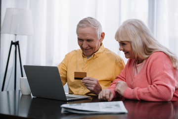 senior couple sitting on couch with laptop and credit card while doing online shopping at home