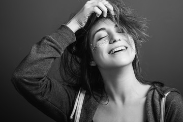 Beaming young woman messing hair. Youth beauty. Playful mood. Toothy smile. Eyes closed. Black and...