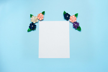 Paper blank with satin flowers and copy space on a blue background. Top view, flat lay. Spring concept