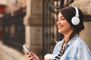 Young woman listens to music via headphones and smartphone in the city