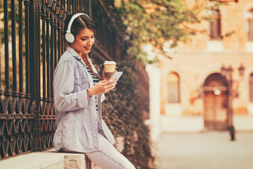 Young woman listens to music via headphones and smartphone in the city