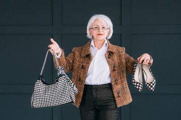 Senior fashion stylist. Personal consultant on trendy wardrobe. Confident aged lady posing with bag...
