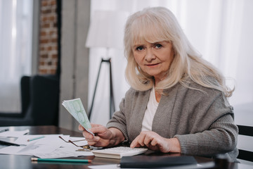 senior woman sitting at table, using calculator and counting money