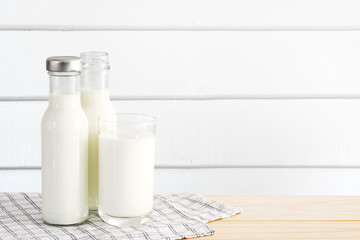 Milk in glass and bottle put on wooden table in white wood wall room.