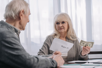 senior couple holding envelope with 'roth ira' lettering and dollar banknote at home