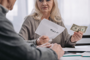 cropped view of senior couple holding envelope with 'roth ira' lettering and dollar banknote