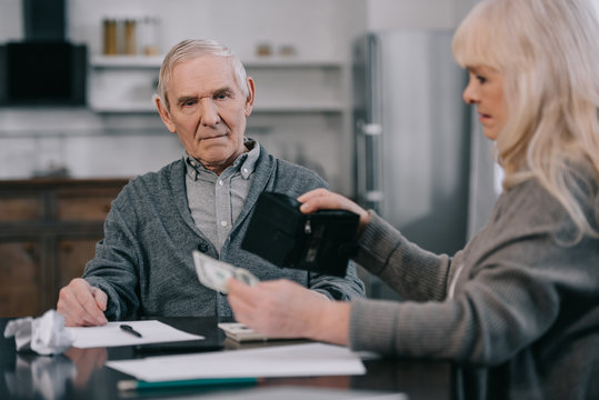 Senior Woman Holding Wallet And Money While Sitting At Table With Man