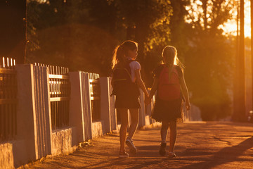Two child girls is walking with a school bag in sunny day