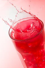 Close up of a splash on a glass of strawberry juice against a red background
