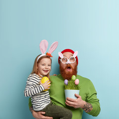 Big day is coming up. Surprised busy father shocked to have much work preparation to Easter, paints eggs together with daughter, pose over blue wall, rejoice spring and holidays. Celebration concept