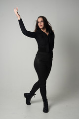 full length portrait of a brunette girl wearing  modern black jacket and pants, standing pose  on grey studio background.