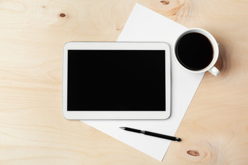 Digital tablet computer and cup of coffee on wooden desk.