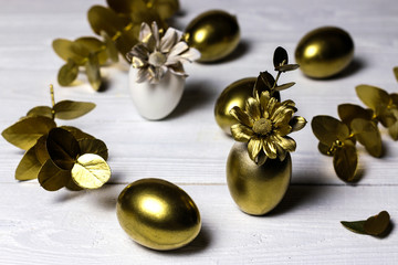 Golden eggs, decorative leaves and flowers on white vintage background.