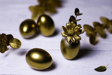 Golden eggs, decorative leaves and flowers on white vintage background.