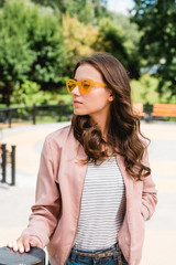 pretty girl in sunglasses standing with hand in pocket in park