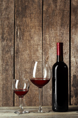 Glass and bottle with delicious red wine on table against wooden background