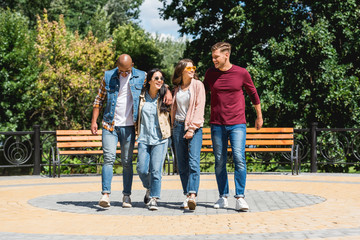 cheerful multicultural group of friends smiling while walking in park