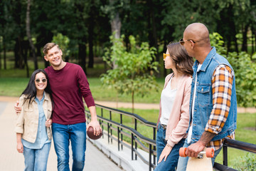 Obraz premium happy man holding american football and walking with girl near multicultural friends