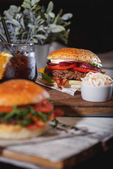 Fresh classic burger with beef, cheese, bacon, onion and lettuce in bun with poppy seeds on wooden table.