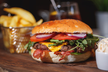 Fresh classic burger with beef, cheese, bacon, onion and lettuce in bun with poppy seeds on wooden table.