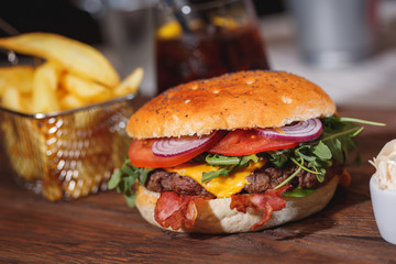 Fresh classic burger with beef, cheese, bacon, onion and lettuce in bun with poppy seeds on wooden table.