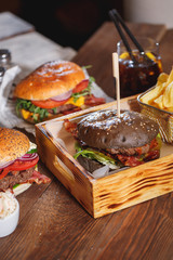Fresh classic burger with beef, cheese, bacon, onion and lettuce in dark bun on wooden table.