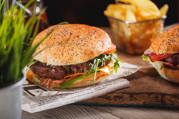 Fresh classic burger with beef, cheese, bacon, onion, tomato and arugula on wooden table.