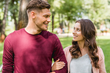 cheerful couple looking at each other while smiling in park