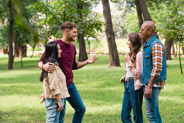 cheerful multicultural friends talking while standing in park