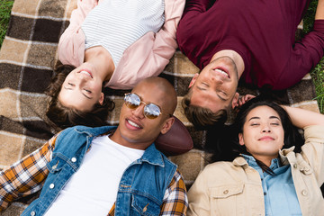 overhead view of happy multicultural friends lying on checkered blanket