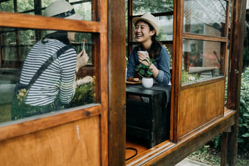 communication and friendship concept. smiling young asian women with tea bowls in chado shop outdoor cafe. girl best friends laughing chatting talking cheerful relax in japanese old wooden house zen