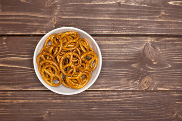 Lot of whole mini salted pretzels in a grey ceramic bowl flatlay on brown wood