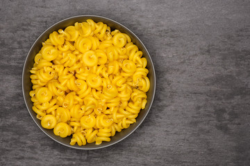 Lot of whole raw pasta funghetto variety in a grey ceramic bowl flatlay on grey stone
